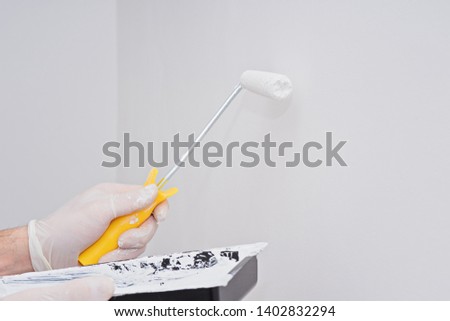 Closeup paint roller in hand with white paint on clean wall with copy space. Mock up template with place for text for painting or moving concept