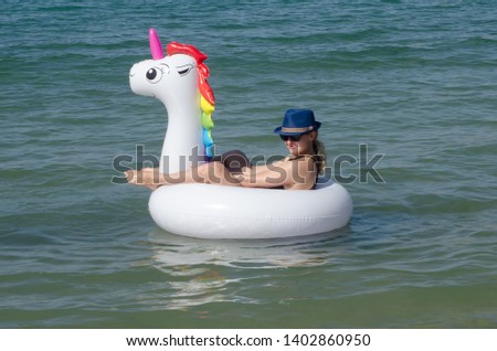 Woman floating on a white beach inflatable unicorn pool in sea
