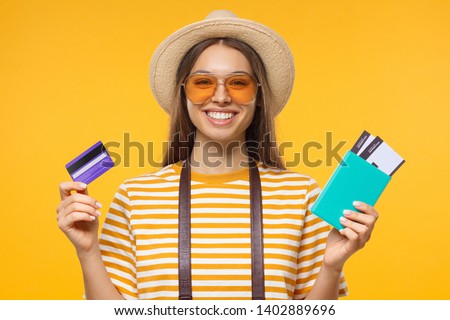 Photo of young European female isolated on yellow background holding credit card and airplane tickets that she bought on sale