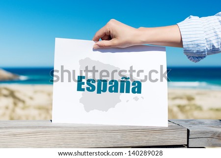 Closeup of woman's hand holding Espana sign at beach
