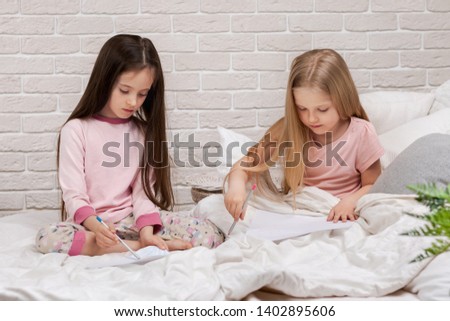 kids drawing pictures while lying on bed. pajama party and friendship.