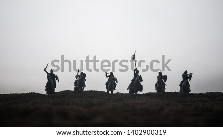 Medieval battle scene with cavalry and infantry. Silhouettes of figures as separate objects, fight between warriors on sunset foggy background. Selective focus Royalty-Free Stock Photo #1402900319