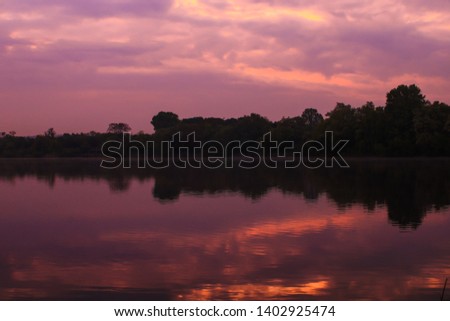 Symmetry of colorful sky in the water at sunset  with forest over the horizon. Dark picture in landscape