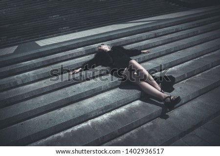 Goth girl in black shorts and black shirt lie on the stairs at street	