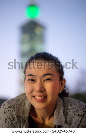 Close up young woman smile and looking to camera of 101 tower Taipei background at night. (Visible noise due to high ISO, soft focus)