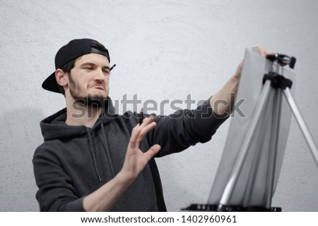 Portrait of satisfying young man painting with pencil on easel