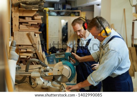 Side view portrait of  carpenter cutting wood using disksaw while working in joinery workshop, copy space