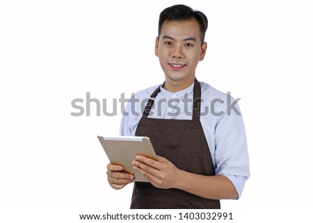 Asian handsome young waiter holding pad tablet, in brown color apron, isolated on white background Royalty-Free Stock Photo #1403032991
