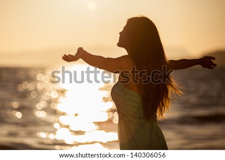 Pretty young woman enjoying a sunset at the beach with arms wide open