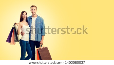 Body photo of happy young couple with shopping bags, with copy space for some slogan or advertising text, over yellow color background. Man and woman - holidays sales, shopping concept studio picture.