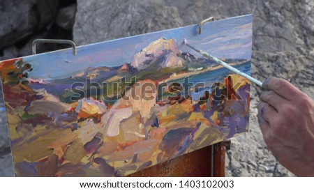 Male artist paints an oil painting on canvas plein air. Seascape, marine landscape. Mountains, rocks and sea