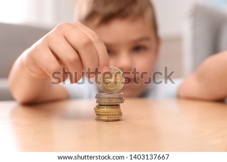 Cute little boy stacking coins at home, focus on hand