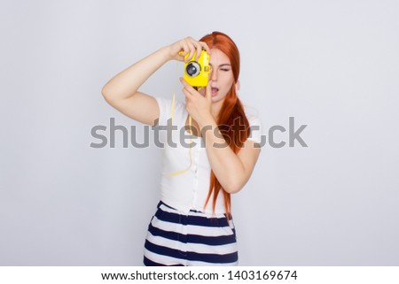 Portrait of a beautiful young redhead woman wearing summer clothing standing isolated over white background, using photo camera