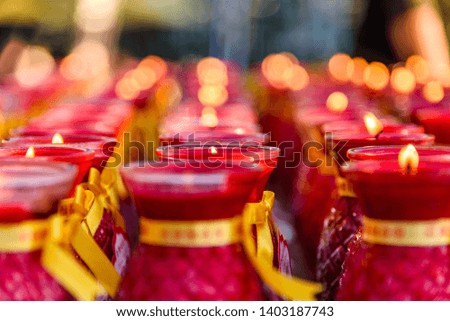 Several rows of red buddhist prayer candles fading into the background. Chinese Translation: "We offer these prayers to the Buddha" 