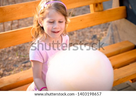 Happy little girl with cotton candy outdoors. Blonde kid holding pink cotton candy.