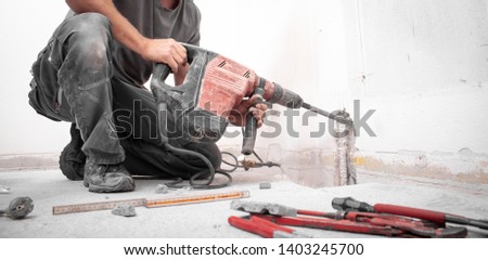 Installer stabs hole with Hilti rotary hammer in the wall on the construction site Royalty-Free Stock Photo #1403245700