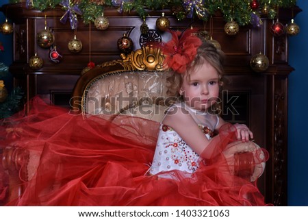 cute little girl in a chair by the Christmas tree in a red smart dress
