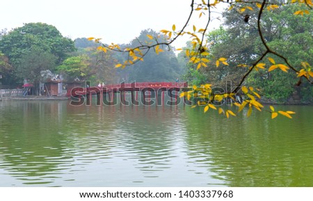 Architectural Huc Bridge looming shake branch leaves trees in lake with arched red crawfish culture symbolizes history thousands years in Hanoi, Vietnam Royalty-Free Stock Photo #1403337968