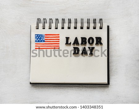 LABOR DAY. Notepad, American flag pattern and wooden letters of the alphabet on a white table. Close-up. Bright photo and space for your inscriptions. Congratulations to relatives, friends, colleagues