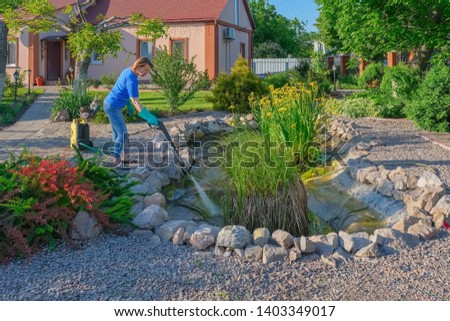 middle-aged white woman cleans a garden pond with high-pressure wash from sludge. 