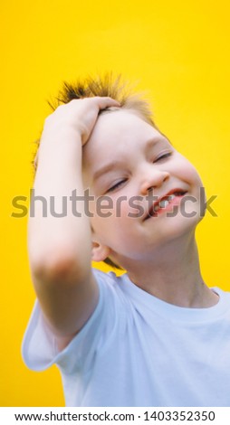 boy runs a hand through his hair while standing against yellow background. happiness and satisfaction concept.