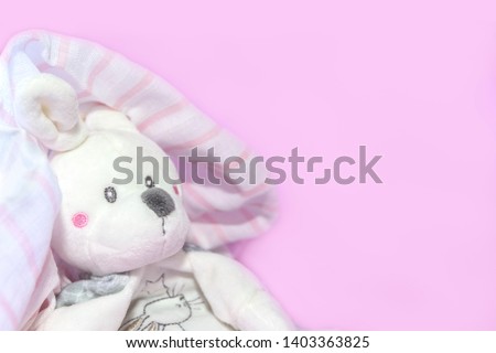 Funny newborn baby toys, teddy hare peeking out from under towel after shower on pink background. Copy space, flat lay, top view.