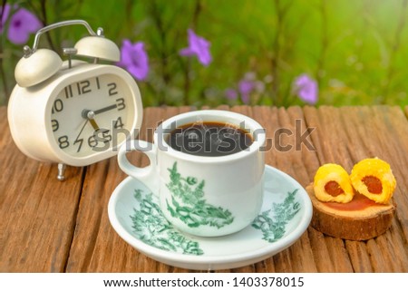 A cup of coffee with alarm clock and  pineapple tart   on old wooden table.
