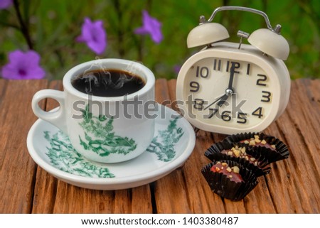 A cup of coffee  with alarm clock , chocolate almond london  in the morning.