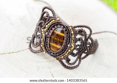 Macrame bracelet with natural mineral tyger eye gemstone on natural wooden background
