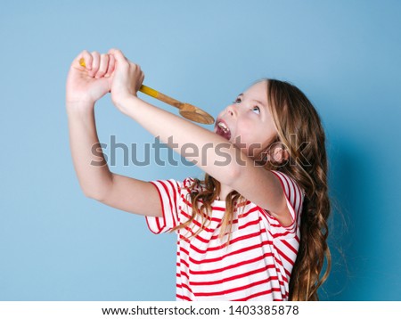 pretty cool and young girl uses cooking spoon as microphone and sings in front of blue background
