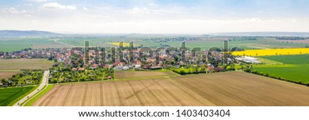 Composite panorama of aerial photos of a village in northern Germany with houses between a cultural landscape with fields and meadows.