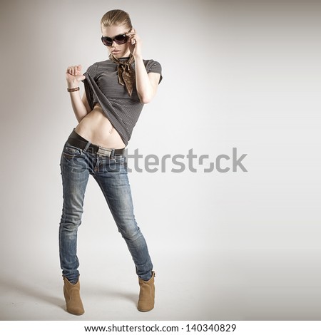 Gorgeous fashion girl in sunglasses wearing stylish jeans and high heels. Beautiful model posing at studio.