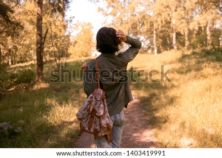 A girl traveler in the wild, a girl with a backpack in the woods, a traveler walks along a forest path, a woman with a bag on her shoulders travels through a wild forest