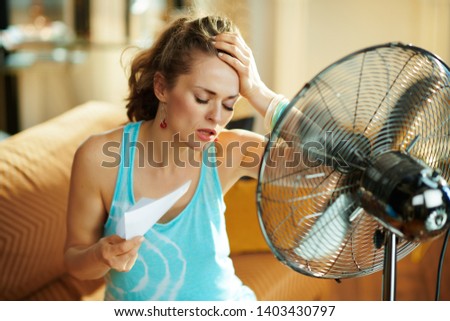 unhappy housewife in the modern house in sunny hot summer day in the front of working fan suffering from summer heat Royalty-Free Stock Photo #1403430797