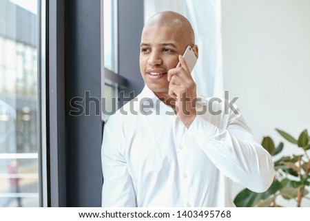 Portrait of handsome African-American man talking by phone in office