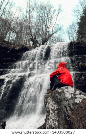 Woman in red jacket sitting by waterfall