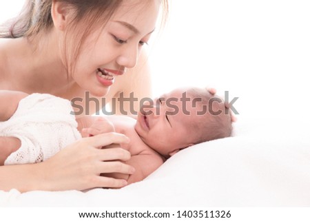 Young attractive mother looking her newborn baby with love and caring, Happy beautiful mother lie down on bed playing together with 0-1 month Asian newborn baby, lifestyle modern mother concept