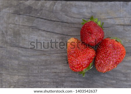Three ripe strawberries on wooden background. Free copy space. Top view.