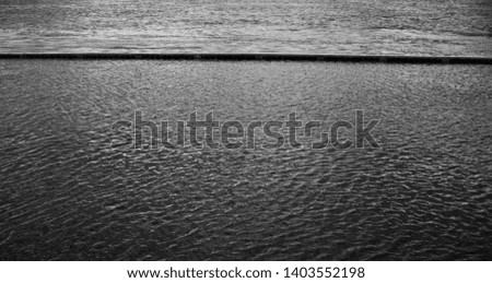 black and white landscape photo of water. The pattern of water. Flood on the river. The embankment is covered with water. A clear horizontal line divides the stream into two parts. 