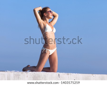 Girl resting on concrete pier. Attractive young woman in sunglasses kneels on concrete wall with hands behind head