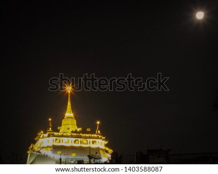 Golden pagoda called Golden Mount at Saket Temple (Wat Saket) at night time with the full moon and black background. A landmark in Bangkok, Thailand.