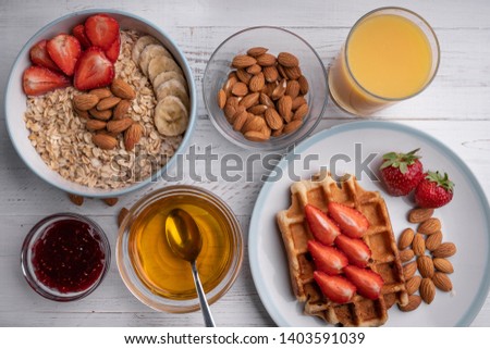 Breakfast menu food top view. Oatmeal, waffles, berry, nuts, cereal, honey, orange juice, strawberry jam on a white table. Delicious menu. Dessert. Ingredients