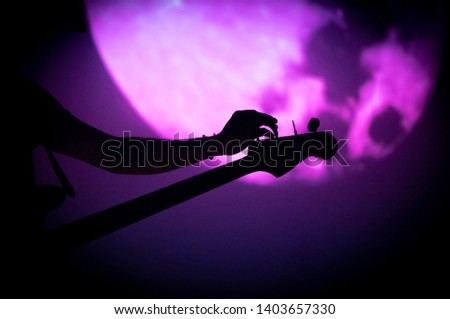 Silhouette of bass guitarist's tuning his instrument during concert with black and purple background
