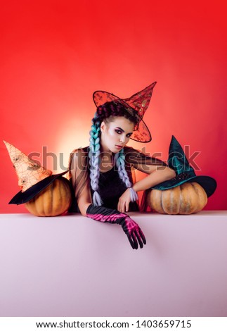 Happy gothic young woman in witch halloween costume with hat standing red background. Beautiful surprised woman in witches hat and costume holding pumpkin. Holidays, decoration and party concept