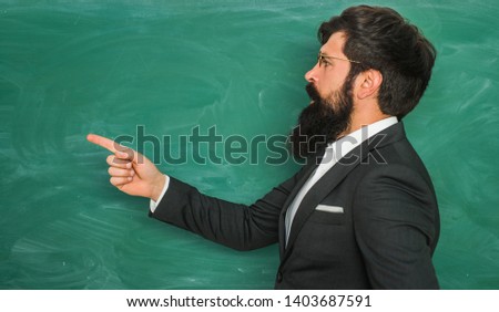 Bearded professor at school lesson at desks in classroom. Education. Chalkboard copy space. Friendly teacher in classroom near blackboard desk