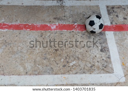 Old ruined damaged soccer ball put on red line  in cracked cement field with sun light. What is broken, nobody is interested. Copy space and concept image.