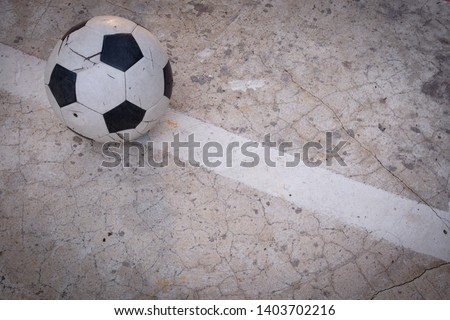 Old ruined damaged soccer ball put on white line  in cracked cement field with sun light. What is broken, nobody is interested. Copy space and oncept image.