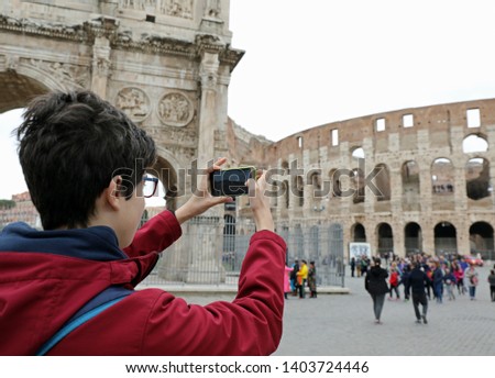 Young boy with glasses takes picture of Colosseum with his smart phone in Rome Italy