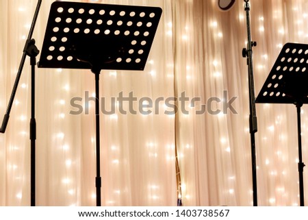 music stands in front of a semi opaque curtain covering strings of starry lights
