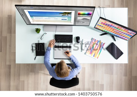 Elevated View Of Female Editor Using Graphic Tablet While Working On Computer In Office